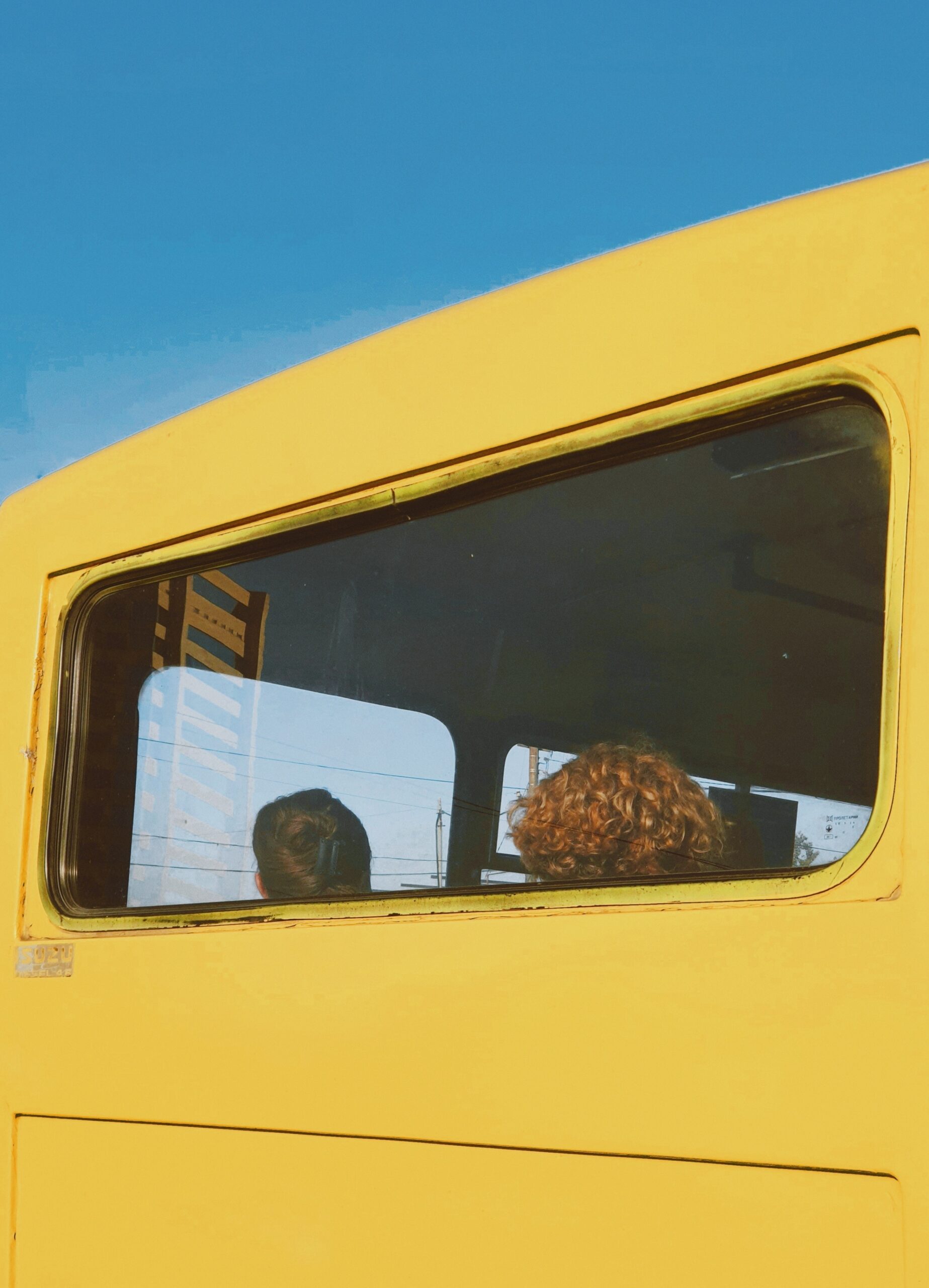 Zuka Kotrikadze — Tbilisi, Georgia. Framed by a battered yellow marshrutka window, two passengers ride through Tbilisi.