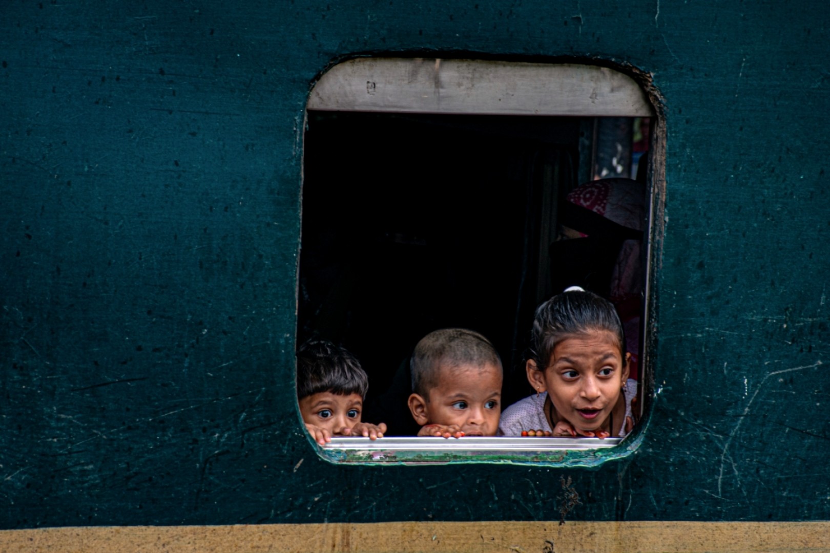 Monsurul Azam — Chattogram, Bangladesh. Three children peer curiously through a train window, their faces lit with excitement and wonder.